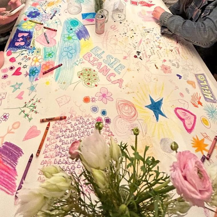 A long paper tablecloth covered in crayon flowers, hearts and stars, crayons scattered across it